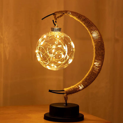 A minimalist crescent moon-shaped table lamp features a suspended glass globe filled with warm LED fairy lights, casting a soft golden glow. With its clean design and cozy lighting, this lamp serves as a stylish decorative piece, perfect for enhancing bedrooms, bedside tables, or modern living spaces.