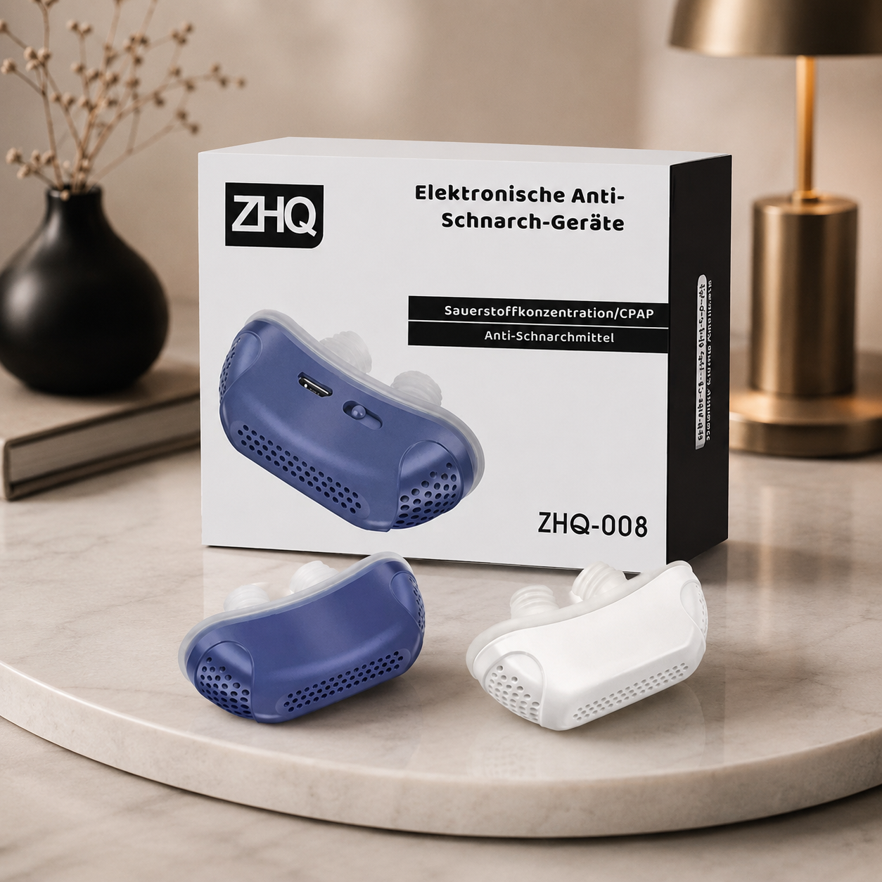 Dieses Bild zeigt die Produktverpackung des elektronischen Anti-Schnarch-Geräts zusammen mit zwei Farbvarianten des Geräts in Dunkelblau und Weiß. Die elegante Präsentation auf einer Marmoroberfläche in einer modernen Wohnumgebung vermittelt einen hochwertigen und stilvollen Eindruck.